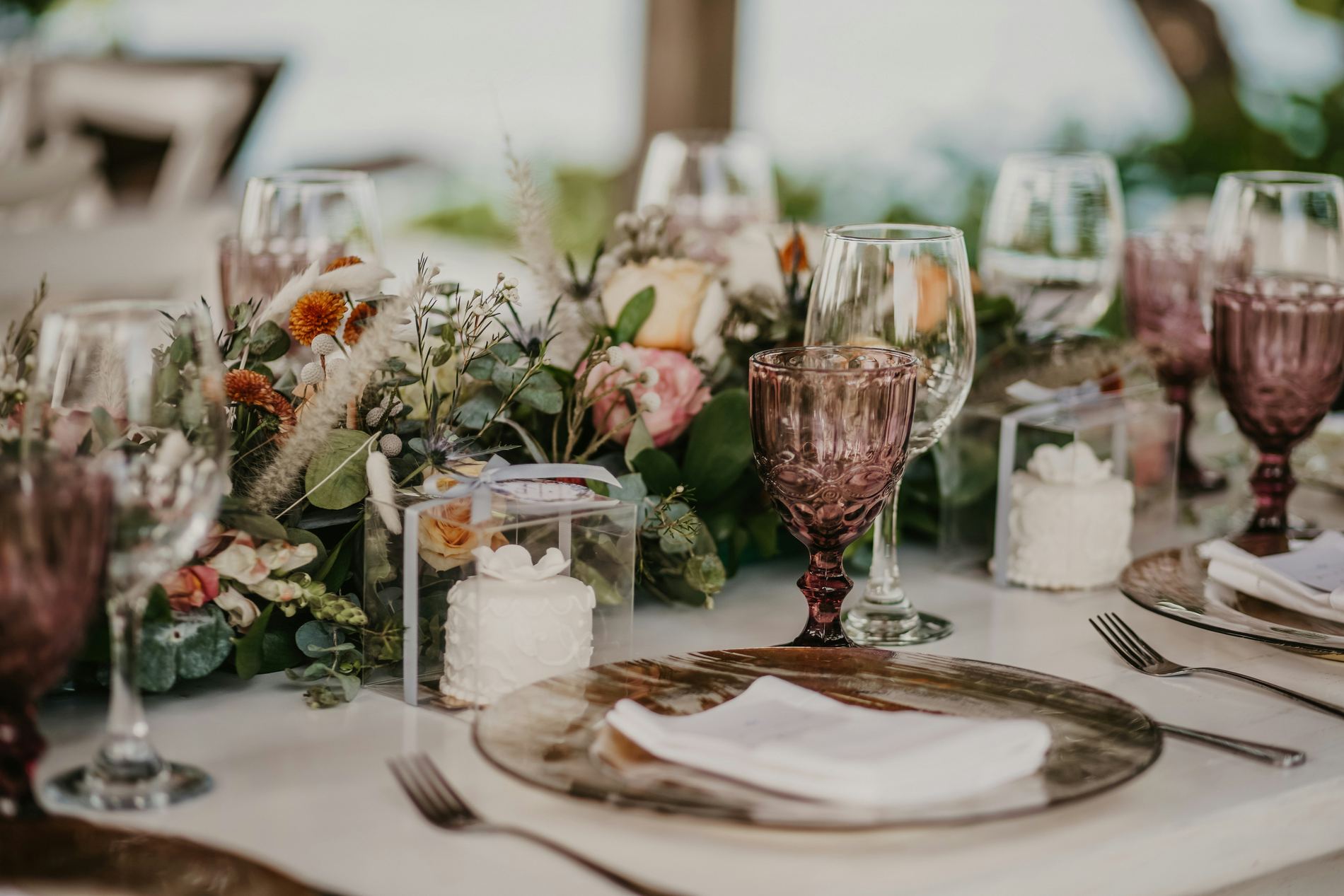 A wedding table set with amber glass, dusty-rose goblets, and trailing greenery.