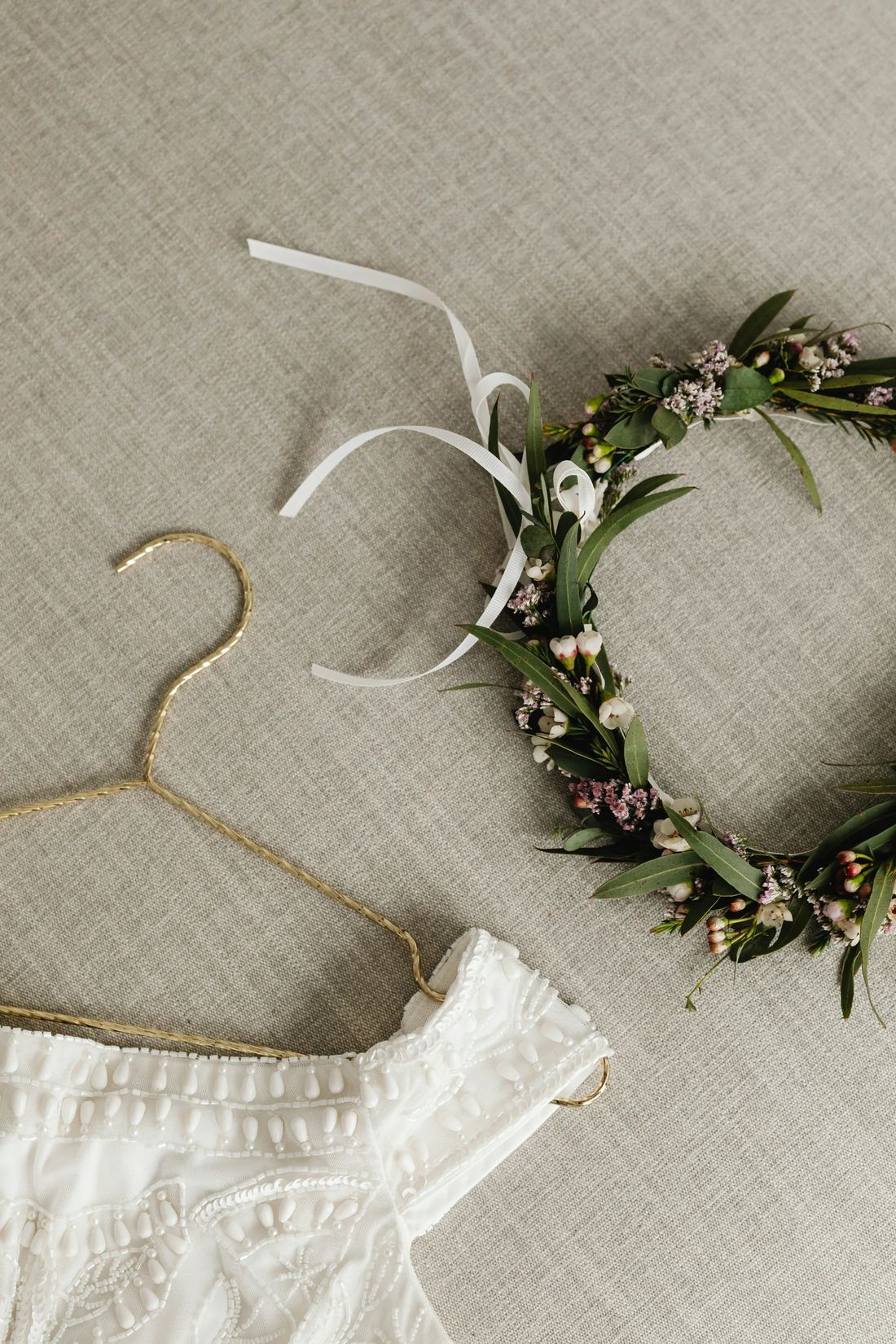 Beaded bridal gown on a gold hanger beside a floral crown.