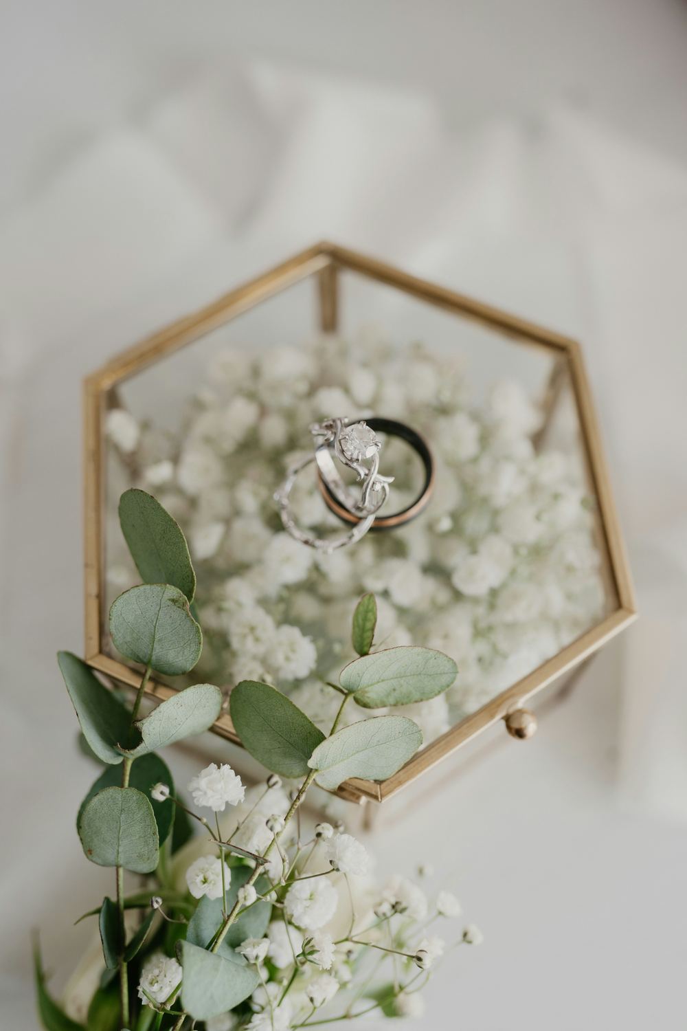 Two wedding bands on a glass keepsake box over baby's breath.